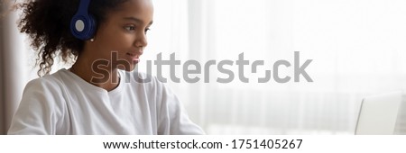 African teenage girl wear headphones use laptop learning language on-line, do school subject tasks at home, distant education, homeschooling concept. Horizontal photo banner for website header design