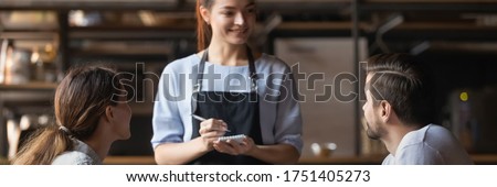 Courteous waitress, small business owner holding notepad ready take restaurant visitors order couple. Eating in public places, good service concept. Horizontal photo banner for website header design