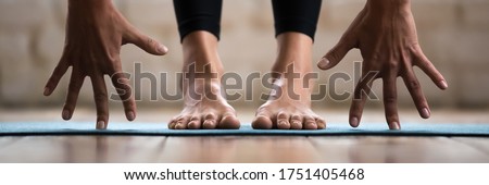 Horizontal photo banner for website header design sportive woman performing forward bend practising yoga uttanasana asana pose. Barefoot legs in pants on yogic mat palms close up view wellness concept