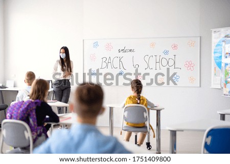 Teacher with face mask welcoming children back at school after lockdown. Royalty-Free Stock Photo #1751409800