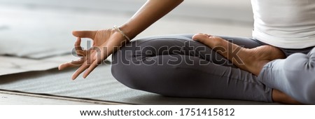 African woman wearing active wear do yoga practice meditating indoors, close up cropped photo lotus position. No stress, mindfulness, inner balance concept. Horizontal banner for website header design Royalty-Free Stock Photo #1751415812