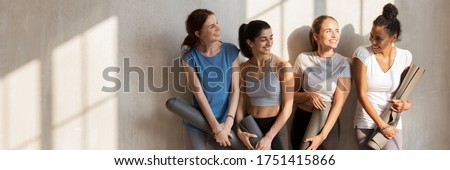 Multi racial girls wear active wear talking standing near wall holding personal mats wait for yoga session, wellness, weight loss, body care concept. Horizontal photo banner for website header design