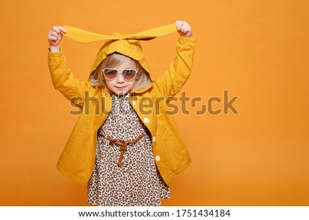 funny girl in yellow raincoat with rabbit ears on yellow background 
