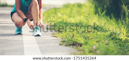 Running woman tying laces of running shoes before jogging through the road in the workout nature park. Weight Loss and Healthy Concept, copy space for banner