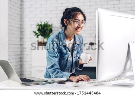 Young smiling happy asian woman relaxing using desktop computer working and video conference meeting online chat.Young creative girl drink coffee at home.work from home concept Royalty-Free Stock Photo #1751443484