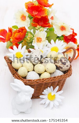 wicker basket with easter eggs, flowers and white rabbit on wooden table, vertical