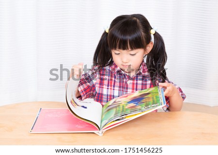 A little girl reading a book in front of white background.