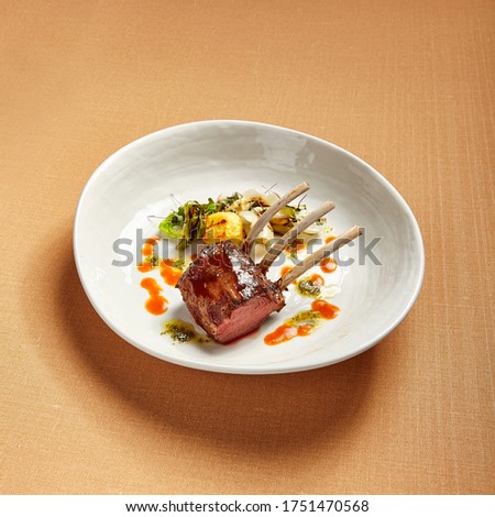 Rack of lamb in white deep plate close-up. Luxury restaurant main course side view. Fancy dish closeup. Mutton ribs. Meat piece served in bowl. Roasted meat with vegetable garnish. Culinary art