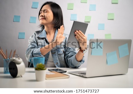 Asian woman annoy looking at tablet reading news showing hand making stop sign at home office. WFH. Work from home. Prevention Coronavirus COVID-19 concept.