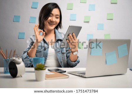 Asian woman happy looking at tablet reading news showing OK sign at home office. WFH. Work from home. Prevention Coronavirus COVID-19 concept.