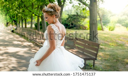 Rear view photo of happy smiling young bride walking away from camera in park.