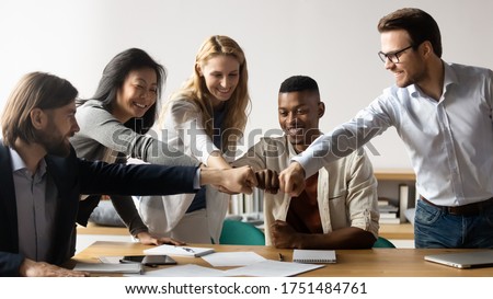 Horizontal image middle-aged and young five multiracial staff members gather in boardroom show unity stacked hands in circle, fists bumping symbol of togetherness common goals business loyalty concept Royalty-Free Stock Photo #1751484761