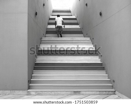Colorful stairs and concrete wall with a man running up to the light. Picture in gray tone.