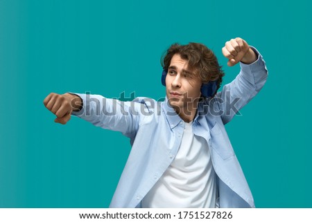 the stretch dance. Portrait of a young beautiful man wearing white t-shirt and blue shirt in headphones dancing and holding fists like bodybuilder