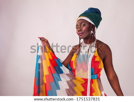 Studio fashion portrait of young African woman in summer dress and ethnic head wrap, white background, sitting girl, high heels