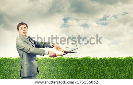 Young handsome businessman cutting green lawn. Greenery concept