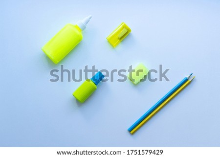 Top view of mixed stationery in yellow and blue colours: glue, sharpener, eraser, two pencils and correction fluid on white background. Concept of education, business, minimalism.