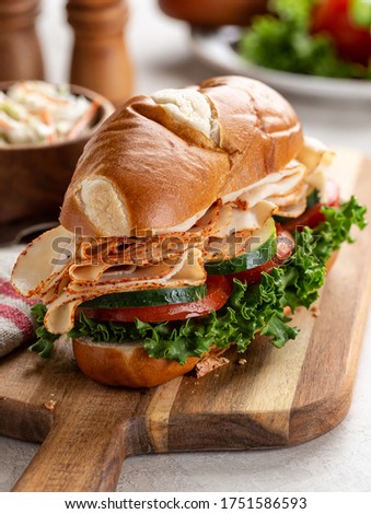 Turkey submarine sandwich with cucumber, tomato and lettuce on a wooden cutting board