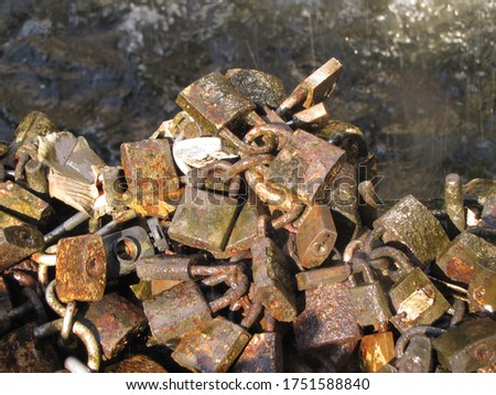 Close-up of several old and worn padlocks with water background of the a fountain of the city of Montevideo. Tradition of locking locks metal padlocks to seal the love of couples, by the sun light.