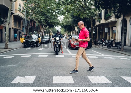 Full body of senior man with backpack in casual wear walking across zebra crossing against blurred cars driving on street Royalty-Free Stock Photo #1751605964