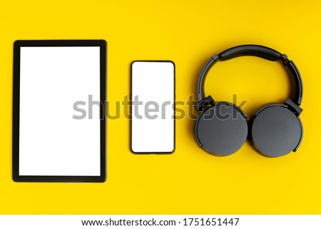 Headphones on plain yellow background with tablet and blank screen phone