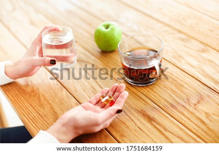 High angle of anonymous female with pills and cup of water witting at table with tea and apple during illness