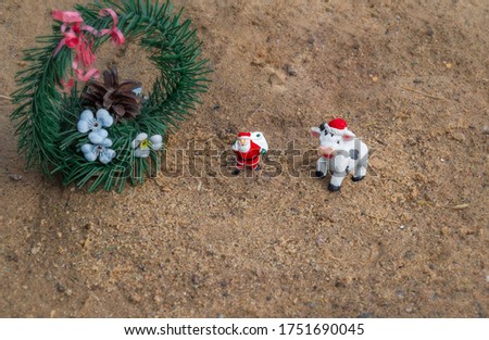 Happy New year 2021. Cow in a Christmas hat. Santa Claus with a bag of gifts. Spruce with a cone. Objects stand on the sand.