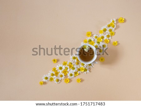 cup of tea among beautifully laid out small flowers of white daisies and yellow buttercups on a beige background. Aromatherapy, natural ingredients, harmony. Good morning wish. Place for text.