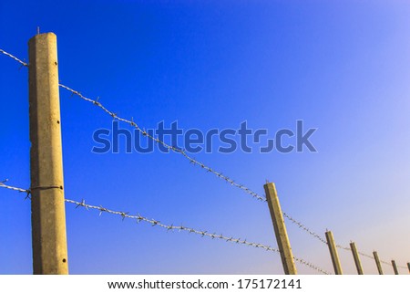 Concrete barbed wire fence with blue sky background