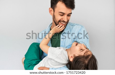 Studio horizontal image of a loving father embraces his cute daughter in his arms. Happy daddy and his little girl playing, cuddling, and enjoying time together on Father's Day. 