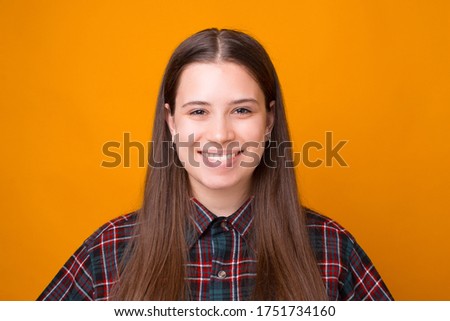 Close up photo of smiling young woman looking confident at the camera, standing over yellow background.