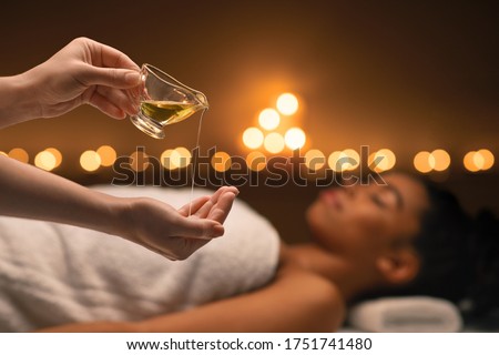 Closeup of female therapist applying massage oil on hands before therapy, young black lady lying on massage table at spa Royalty-Free Stock Photo #1751741480
