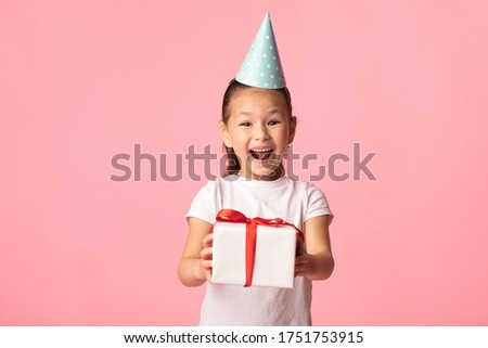 It's For You. Joyful asian kid wearing blue party hat and holding present with red ribbon, posing at studio, free space