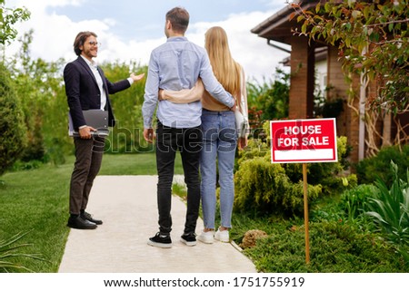 Confident real estate broker showing house for sale to young couple, outside
