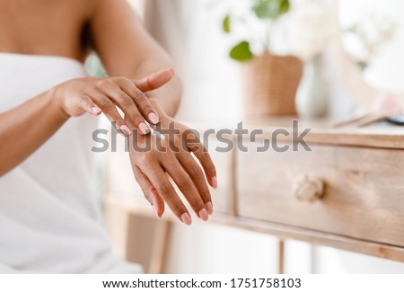 Unrecognizable Black Woman In White Bath Towel Applying Body Milk On Hands, Moisturizing Skin, Sitting Near Dressing Table In Bedroom, Free space