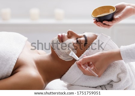 Aesthetic Procedure. Beautician Applying Clay Face Mask On Black Woman Face, Side View Royalty-Free Stock Photo #1751759051