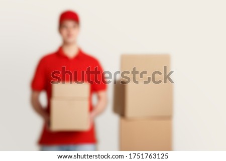 Blurry photo of courier in red uniform, holds parcels, near stack of boxes