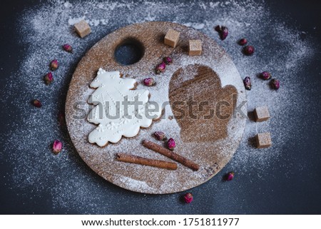 One Christmas gingerbread cookie in the shape of a Christmas tree is on a tray along with cinnamon sticks. From the second cookie in the shape of a mitten remained a silhouette.