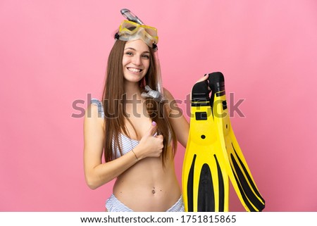 Young caucasian woman holding fins and diving goggles isolated on pink background with thumbs up because something good has happened