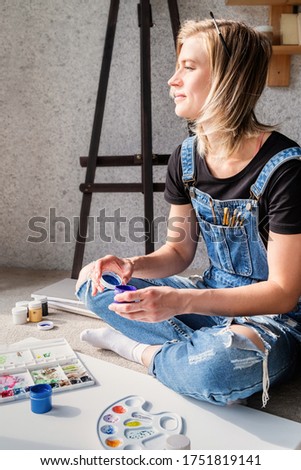 Young woman artist painting a picture at home sitting on the floor