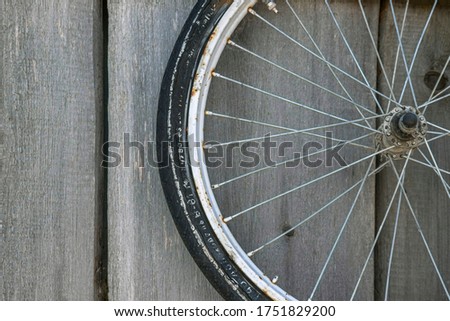 An old bicycle wheel hangs on a wooden fence.