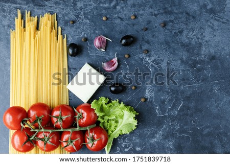 Spaghetti made from durum wheat and ripe cherry tomatoes on a branch, garlic and spices. Fresh greens on a dark graphite background. Products for making delicious pasta. The view from the top.