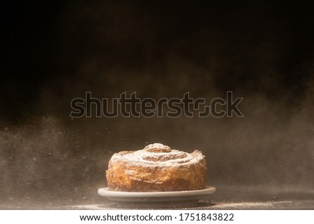 Icing sugar is sprinkling over fresh bundt cake. Freezing motion. Copy space, black background. Bakery concept. Sweet bread on a white plate on a black background.