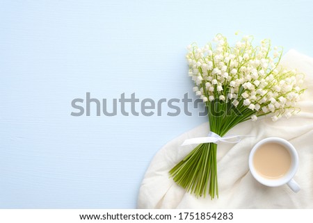Coffee mug with bouquet of flowers lily of the valley on blue rustic table. Flat lay, top view. Beautiful breakfast, good morning concept.