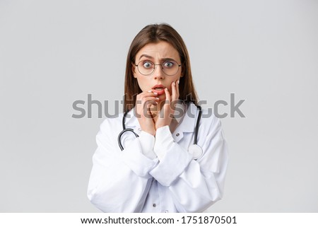 Healthcare workers, medicine, insurance and covid-19 pandemic concept. Shocked scared and concerned female doctor in white scrubs and glasses listening to scary news, gasping, hold hands near lips