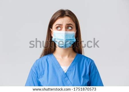 Covid-19, preventing virus, health, healthcare workers and quarantine concept. Skeptical distressed female nurse or doctor in blue scrubs, medical mask, look upper left corner uncertain or puzzled
