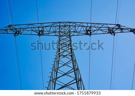 Low angle shot from below to the top of an electricity pylon against blue sky.