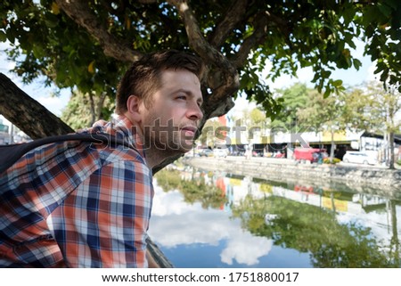 Young caucasian an sitting on the embankment of a river in the city in Thailand.