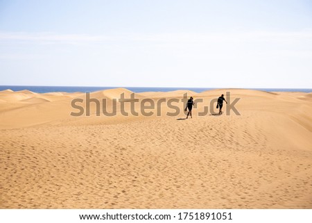 people walking on sand hills near Atlantic ocean against clear blue sky in Maspalomas, Gran Canaria