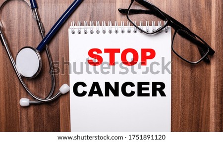 STOP CANCER - an inscription on a spruce sheet that lies on a wooden table between a stethoscope and glasses